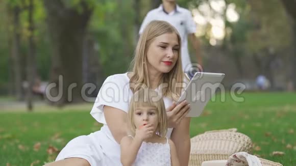 漂亮的高加索女人和她的两个孩子花时间在户外女人用她的药片女儿坐在附近视频的预览图