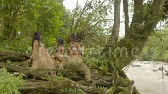制作种子项链的土著妇女在树根之间拍摄视频的预览图