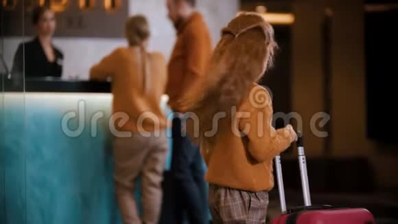 一家人在豪华酒店登记一个小女孩看着镜头在接待处走到她的父母身边视频的预览图