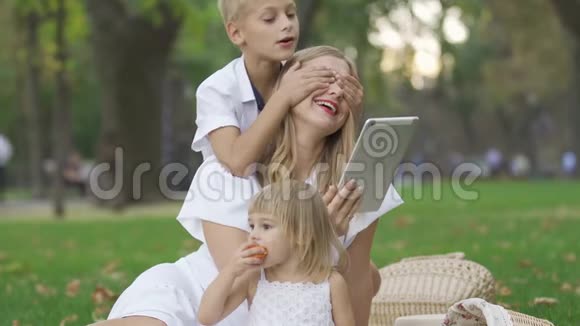 幸福的高加索家庭在公园里度过时光的肖像小男孩遮住妈妈的眼睛而小女孩视频的预览图