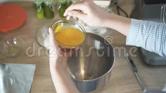 女人的手把盘子里的蛋黄倒进搅拌机的碗里视频的预览图