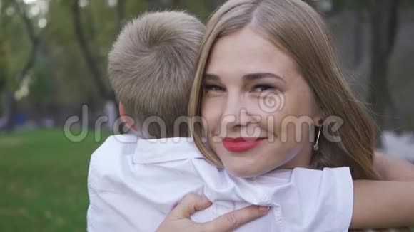 一幅迷人的白种人女人看着镜头拥抱着金发小男孩微笑着的肖像妈妈花时间视频的预览图