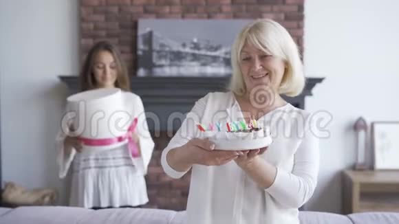 快乐的高级女人向镜头展示蛋糕微笑着站在后台的年轻女子视频的预览图