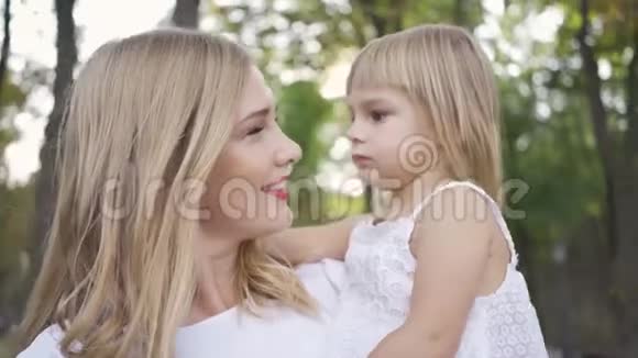 年轻的金发女人穿着白色的抚摸她可爱的女儿女儿拥抱她的母亲户外休闲家庭幸福一个视频的预览图