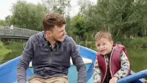 可爱的小男孩握着桨帮助他年轻的父亲划船快乐的年轻父亲和他的小儿子玩得很开心可爱的小爸爸视频的预览图