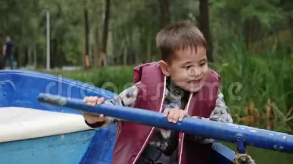小可爱的男孩坐在木船上在城市公园的湖面上划桨可爱的孩子试图在湖上划船关门视频的预览图