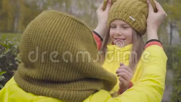 成年白种人女人在小女孩头上戴芥末帽母亲和女儿穿着黄色外套笑着视频的预览图