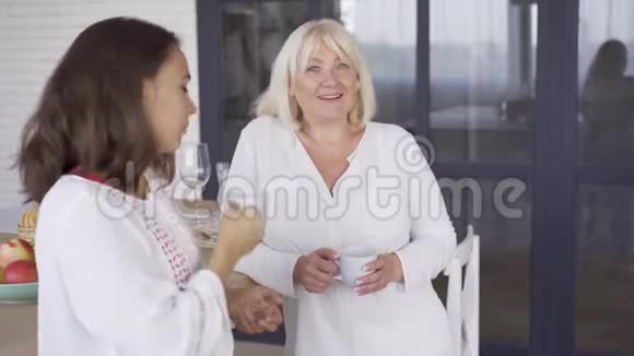 两个女人在厨房里喝茶或咖啡妈妈和多瑟在一起家庭成员分享视频的预览图