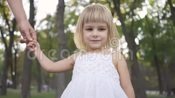 一个穿着白色裙子的小女孩站在公园或森林里牵着成年女人的手摇着她的手快乐视频的预览图