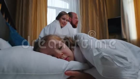 旅馆房间里的一家人一个睡在床上的小女孩她的父母打开窗帘女孩醒来了视频的预览图