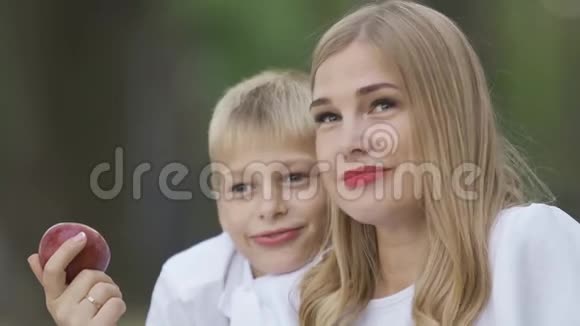 漂亮的金发女人和小男孩坐在一起手里拿着苹果说话妈妈和儿子在一起视频的预览图