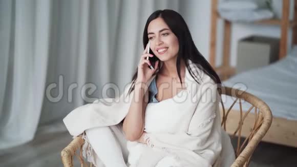 漂亮的女孩坐在客厅的藤椅上打电话笑视频的预览图