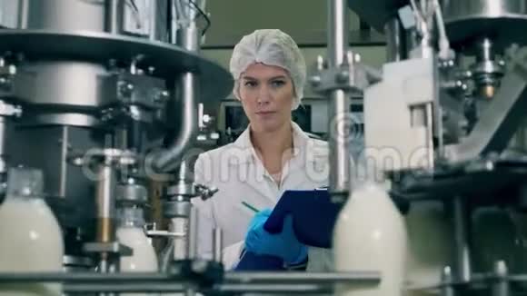 女人在工业食品和饮料厂传送带上检查牛奶瓶子视频的预览图