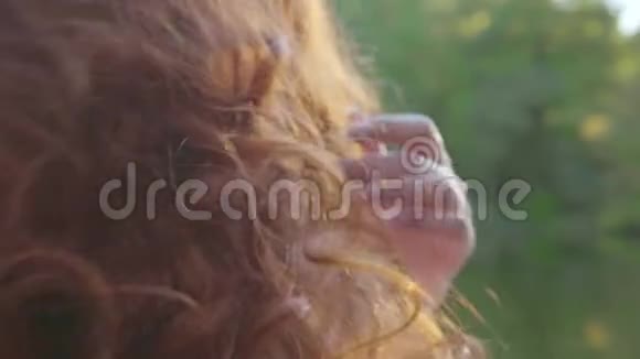 一位年轻的白种人女子在湖畔的阳光下抚摸着她的红色长发沐浴着阳光视频的预览图