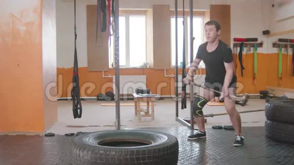 室内运动训练一名带保护膝垫的男子在健身房用金属锤击一个大轮胎视频的预览图
