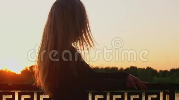 夕阳西下美丽的金发女郎站在河边站在旁转过身来视频的预览图