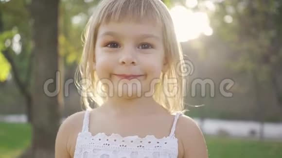 特写一个可爱的金发女孩看着镜头笑了起来阳光下公园里美丽孩子的画像视频的预览图