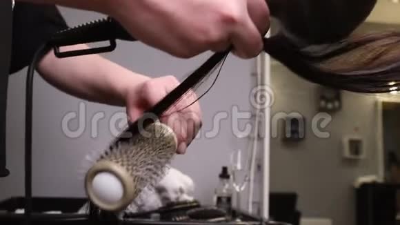 用吹风机和圆刷把理发师的手擦干金色的长发视频的预览图