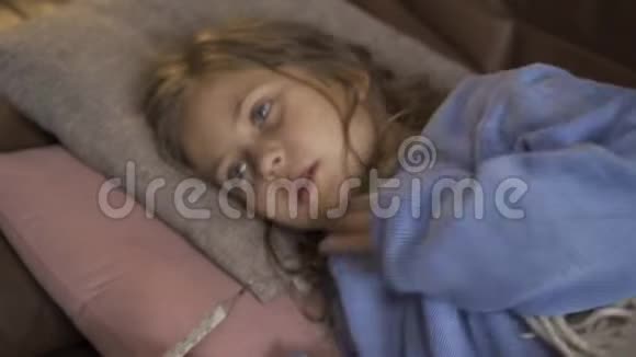 年轻的小女孩穿着蓝色温暖的毛衣带温度一个悲伤的孩子发烧躺在家里的特写镜头视频的预览图
