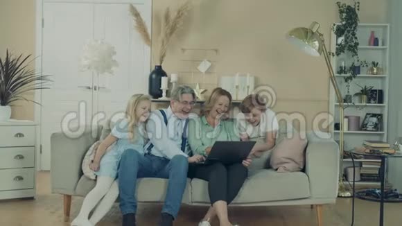 祖父母和他们的孙子孙女们正在家里用笔记本电脑休息视频的预览图