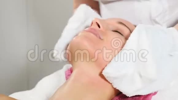 美的概念美容师用湿毛巾从面膜的残留物中清洗一个漂亮女孩的脸视频的预览图