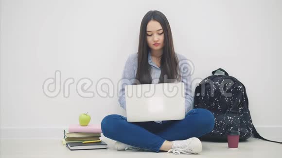 一位年轻的亚洲女士坐在地板上坐在洛托斯的位置上拿着笔记本电脑不明白什么耸了耸肩视频的预览图
