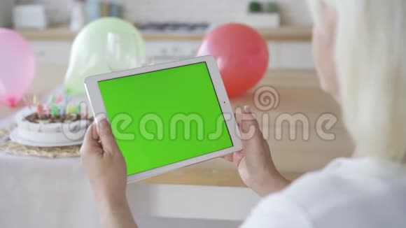 成熟女人手中拿着绿色屏幕的白色平板电脑生日庆典铬化拍摄了视频的预览图