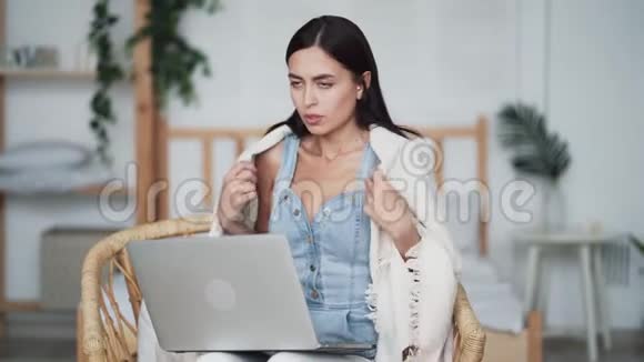 女人冻僵了把自己裹在格子布里女孩坐在椅子上用笔记本电脑工作视频的预览图