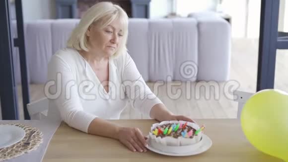 伤心的不快乐的成熟的女人坐在EMLPY房间的小生日蛋糕前的桌子旁然后站起来走着视频的预览图