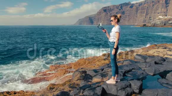 女性金发博主influencer使用万向节稳定器在智能手机上拍摄冲浪视频在火山上视频的预览图
