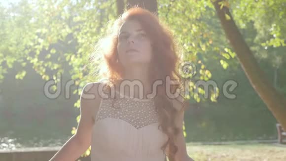 美丽的苗条的白种人妇女的肖像她穿着米色连衣裙站在公园或花园的阳光下视频的预览图