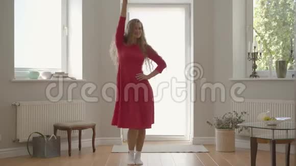 美丽微笑的白种人女人一头长长的卷发穿着红色的连衣裙在家跳舞年轻漂亮的女孩视频的预览图