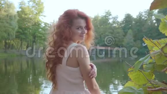 红发少女转身对着镜头笑一个美丽的白种人女人坐在湖畔视频的预览图
