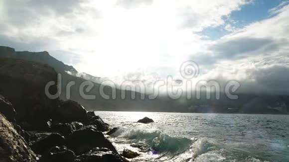 在多云的天空太阳和岩石的背景下黑海的波浪缓慢地撞击着海岸的石头视频的预览图