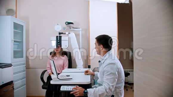 眼科治疗年轻的微笑妇女与医生一起用验光设备检查视力视频的预览图