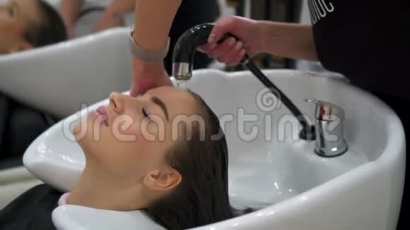 理发师在美容店里洗黑发美女的头发视频的预览图