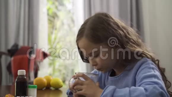 特写一个可爱的小白种人女孩喝着绿茶微笑着桌上放着药丸柠檬和橘子视频的预览图