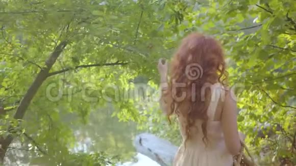 一个红发白种人女孩在树间行走年轻迷人的仙女转向相机微笑视频的预览图