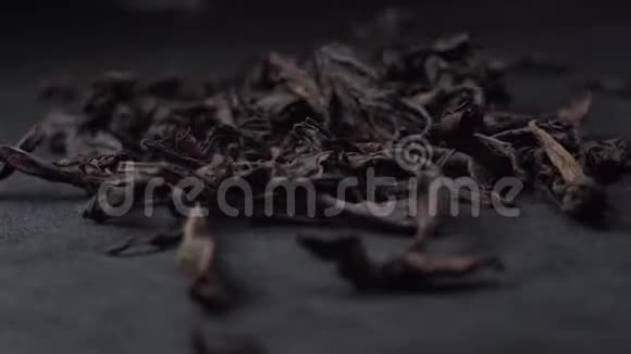 黑色或绿色的茶叶落在黑桌上茶的花瓣旋转的黑色背景视频的预览图