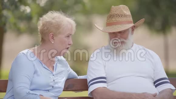 老白种人夫妇坐在夏季公园的长凳上聊天戴草帽的成熟男人视频的预览图