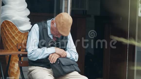 一个戴着帽子的白发老人坐在街上的椅子上睡觉4k4k录像60英尺视频的预览图