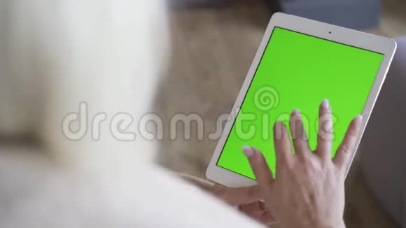 一个拿着绿色屏幕的白色平板电脑的女人的手女人坐着看着平板电脑使用小玩意的金发女人视频的预览图