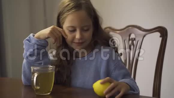 小女孩喝凉茶时拿着柠檬的特写镜头孩子坐在家里的桌子旁小孩喜欢喝茶视频的预览图