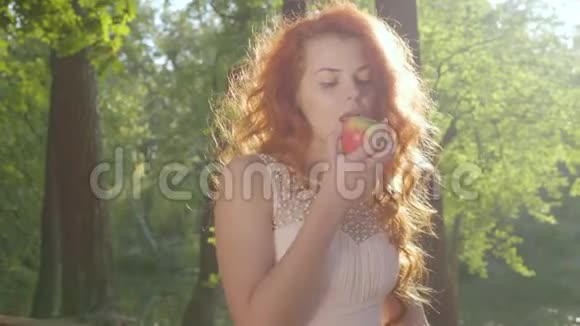美丽的白种人女人穿着白色的衣服在秋天的公园里吃红苹果特写镜头视频的预览图