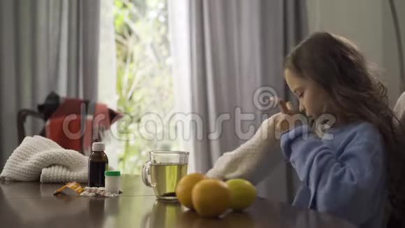 小女孩在家里坐在桌子旁戴着冬帽和围巾的特写镜头啤酒柠檬橘子和视频的预览图
