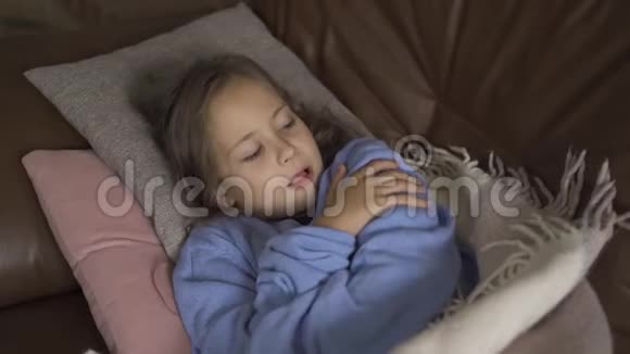 年轻的白种人黑发女孩穿着蓝色毛衣躺在温暖的毯子下咳嗽有发烧的小孩视频的预览图