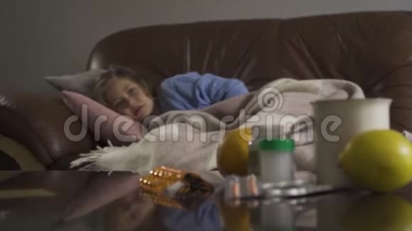 小悲伤的女孩躺在家里的毯子下在后台咳嗽上面有药片柠檬和一杯茶视频的预览图