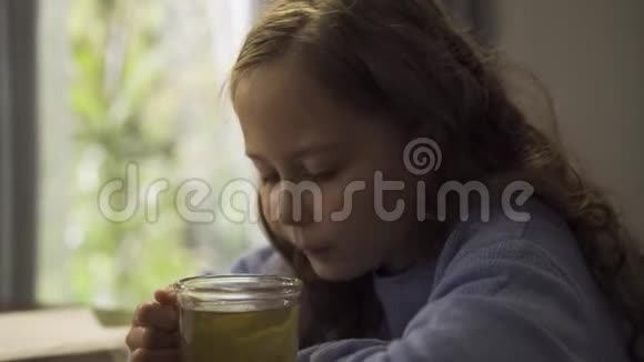 坐在厨房的桌子旁喝绿茶的漂亮小女孩早上喝茶的白人孩子视频的预览图
