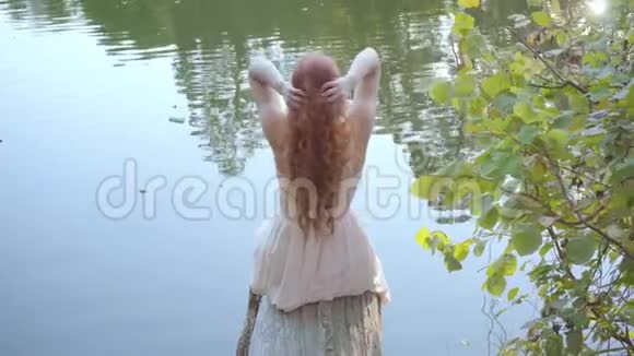 白种人女人抚摸着她的红色长发沐浴在湖畔的阳光中视频的预览图