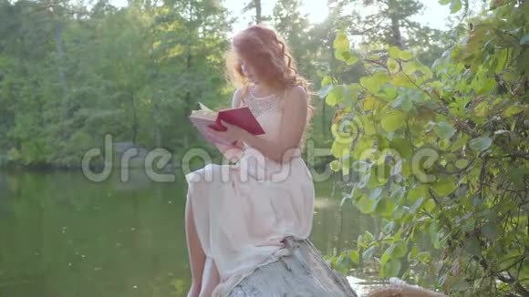 美丽苗条的白种人女人红头发坐在河岸上看书户外休闲教育视频的预览图